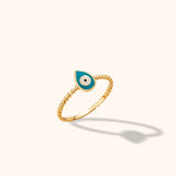 Close-up of a delicate 14K yellow gold beaded band ring featuring a turquoise enamel evil eye motif against a neutral background.
