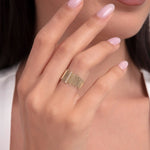 Close-up of a woman's hand wearing a wide 14K gold ring with vertical baguette-style bar detailing in a contemporary design