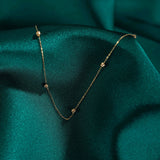 Minimalist 14K solid gold necklace with round beads spaced along a fine chain, on emerald green satin