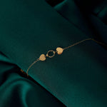 Minimalist 14K gold bracelet with two heart charms and a twisted circle link on green satin background – romantic fine jewelry for her