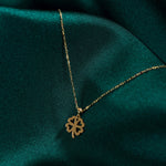 14K solid gold four-leaf clover necklace on green satin background, symbolizing luck and elegance