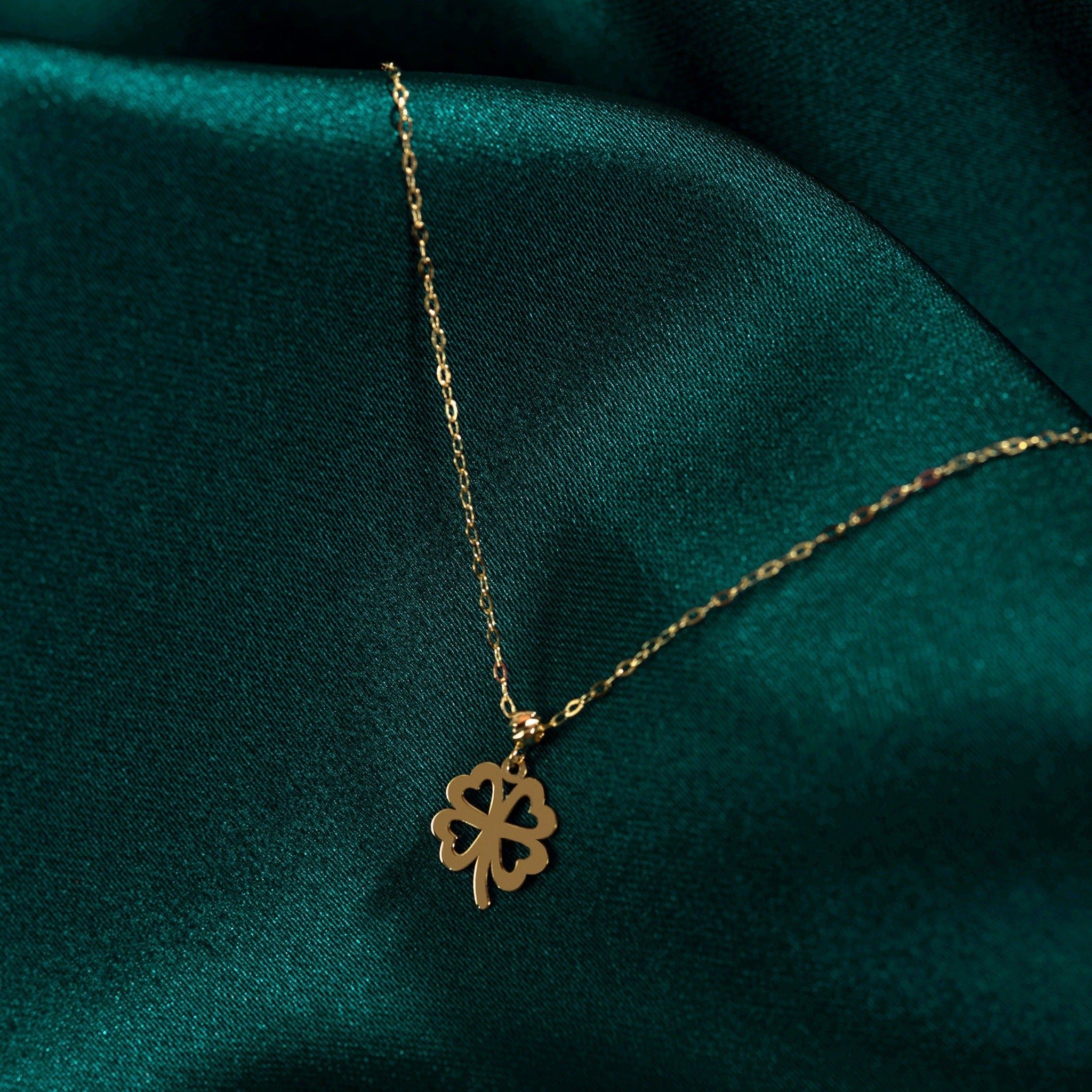 14K solid gold four-leaf clover necklace on green satin background, symbolizing luck and elegance