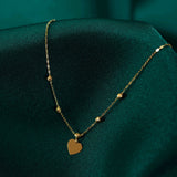 14K gold heart pendant necklace with beaded chain displayed on emerald green satin fabric.