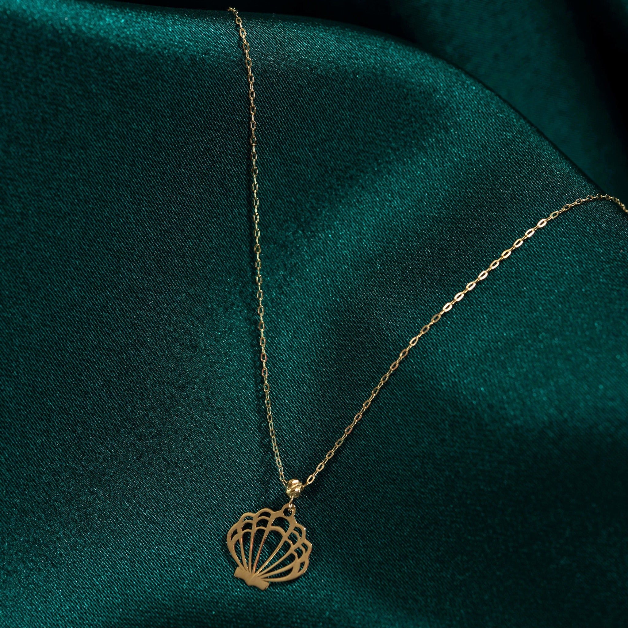 14K solid gold necklace featuring a delicate seashell pendant on an emerald green satin background
