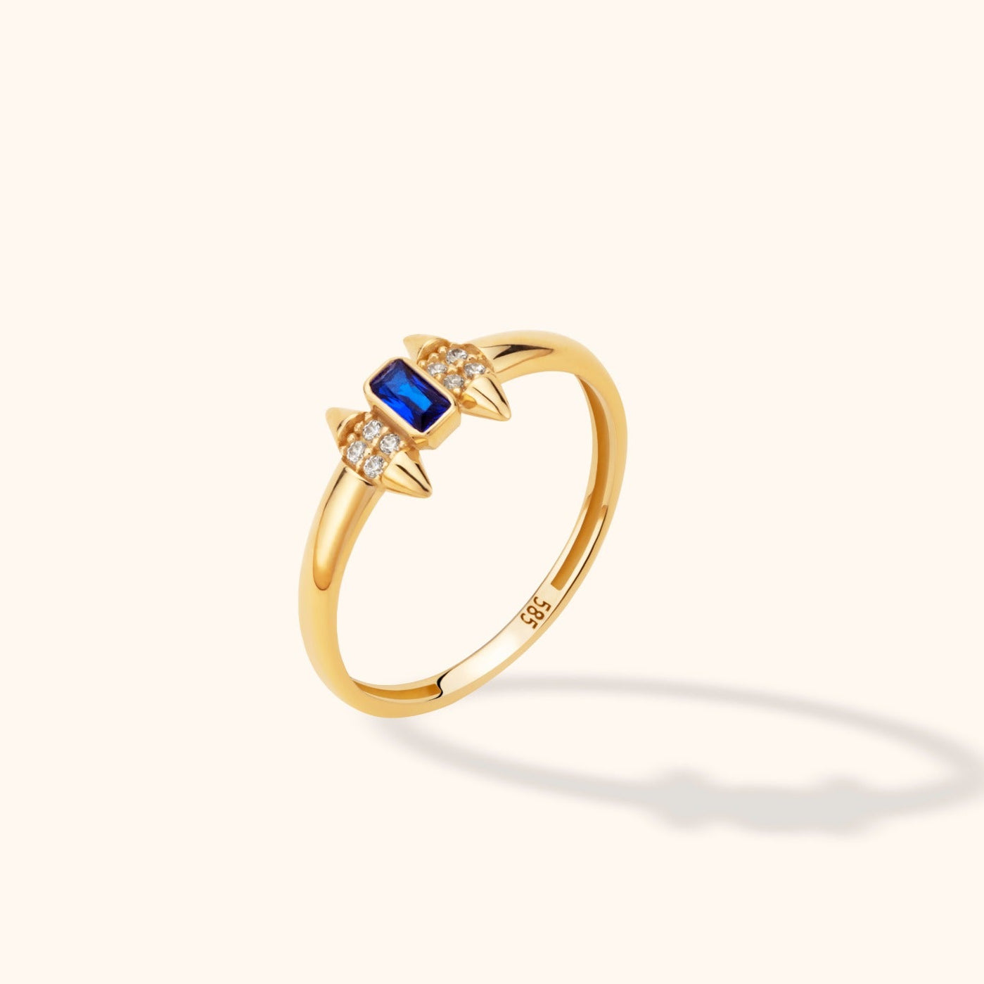 14K yellow gold stackable ring with a blue baguette-cut sapphire, round brilliant diamonds, and spike accents on a neutral background