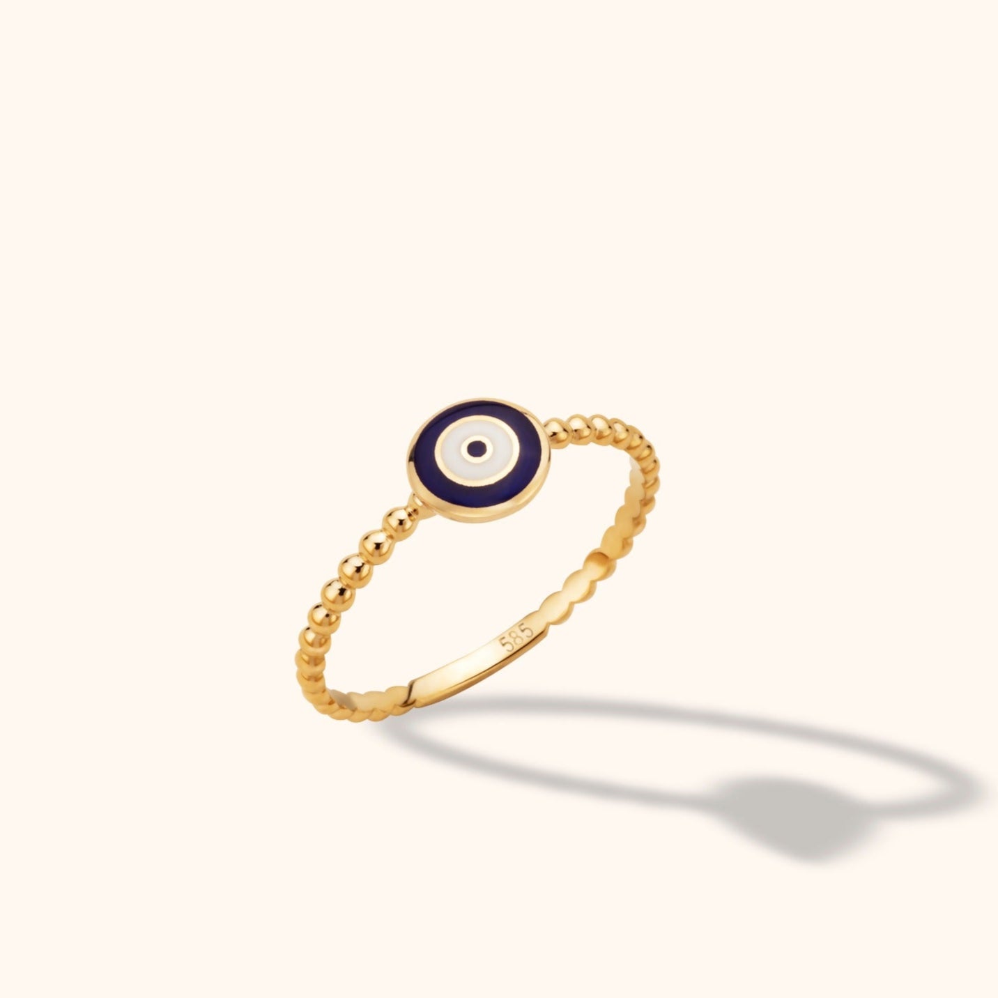 14K yellow gold beaded band ring with a blue and white enameled Evil Eye charm on a neutral background