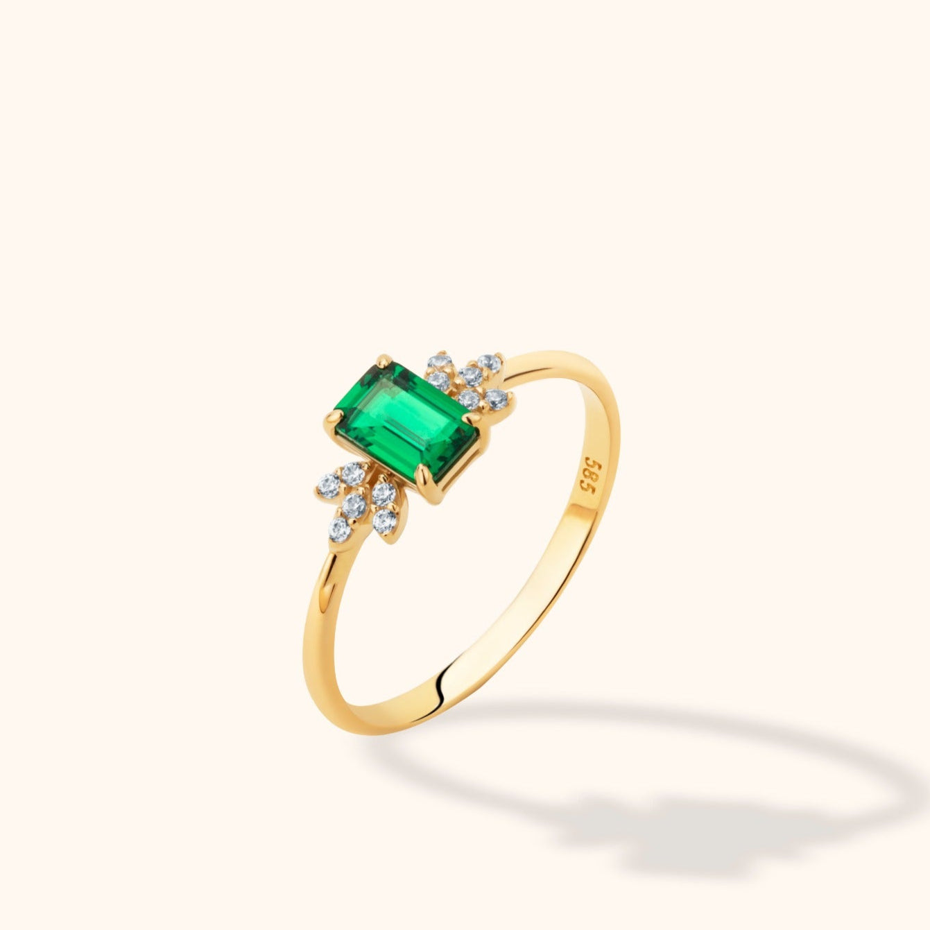 14K yellow gold ring with an emerald-cut green stone flanked by round diamond clusters on a neutral background