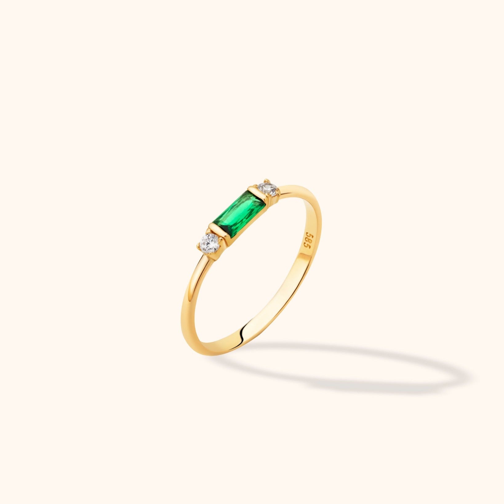 14K yellow gold stackable ring featuring an emerald-cut green baguette center and round diamond accents on a neutral background