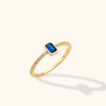 14K yellow gold band ring with an emerald cut blue sapphire center and diamond pavé accents on a neutral background