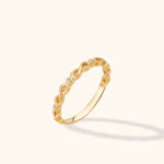14K yellow gold infinity twist ring with pavé diamonds on a neutral background