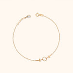Gold-tone chain bracelet with two crosses flanking a textured open circle, an extender chain and a round clasp on a cream background.