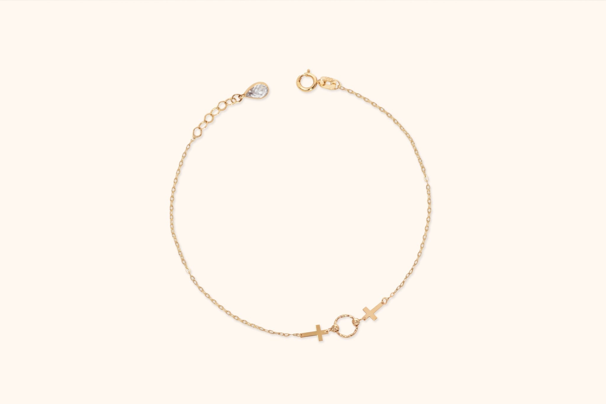 Gold-tone chain bracelet with two crosses flanking a textured open circle, an extender chain and a round clasp on a cream background.