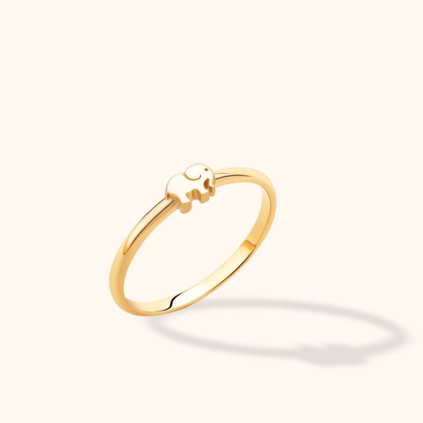 Slim, polished gold-colored ring with a small elephant motif, shown at an angle against a cream background.