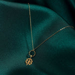 Gold-tone chain necklace with an openwork four-leaf clover hanging from a textured ring, resting on dark green fabric.