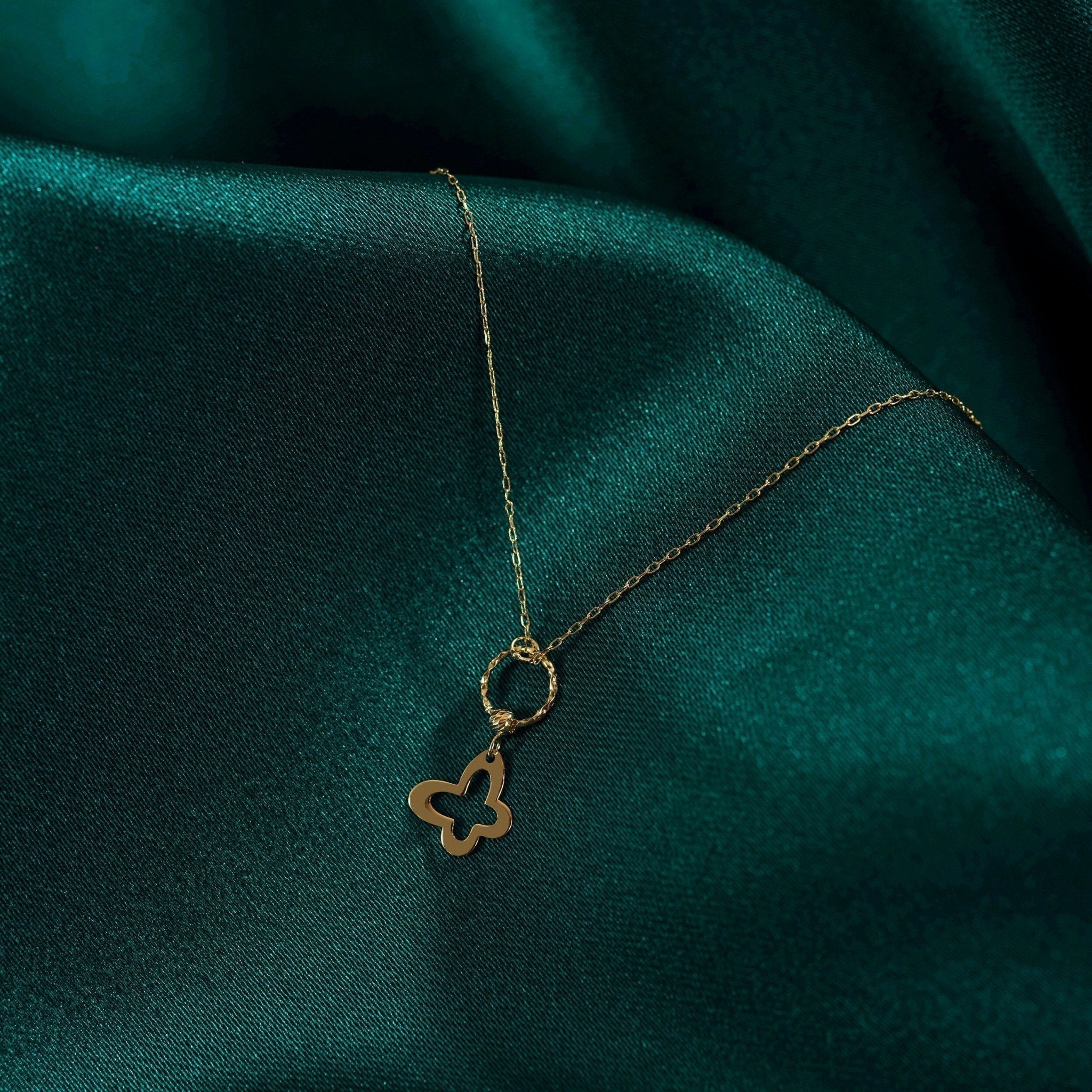 Gold-colored chain necklace with an open butterfly-shaped pendant hanging from a twisted circular ring on dark teal fabric.