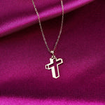 Gold-tone necklace with an open geometric cross pendant and fine oval-link chain on folded magenta fabric.