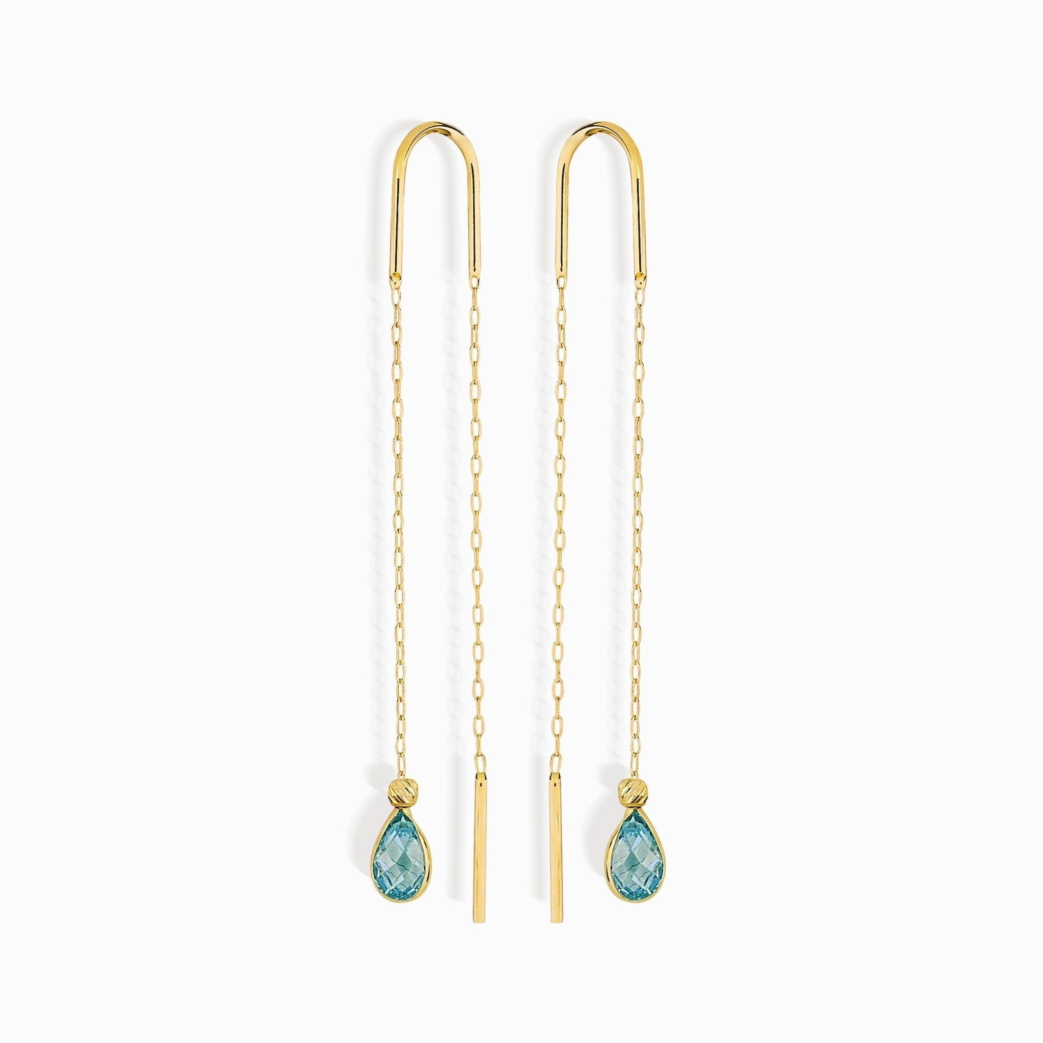 Pair of gold-toned threader earrings with long chains, slim bar ends and faceted blue teardrop pendants on a white background.