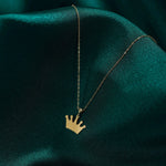 Gold-toned necklace with a flat, five-point crown pendant on a fine oval-link chain, resting on dark teal fabric.