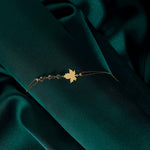 Gold-tone chain bracelet with a flat maple leaf centerpiece and three round faceted accents on dark green fabric.
