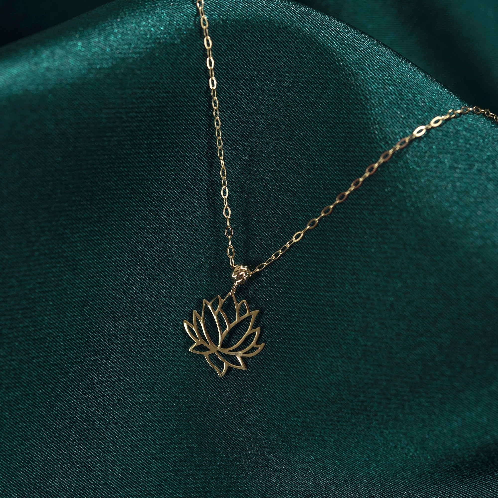 Gold-toned necklace with an openwork lotus flower pendant and oval-link chain resting on dark teal fabric.