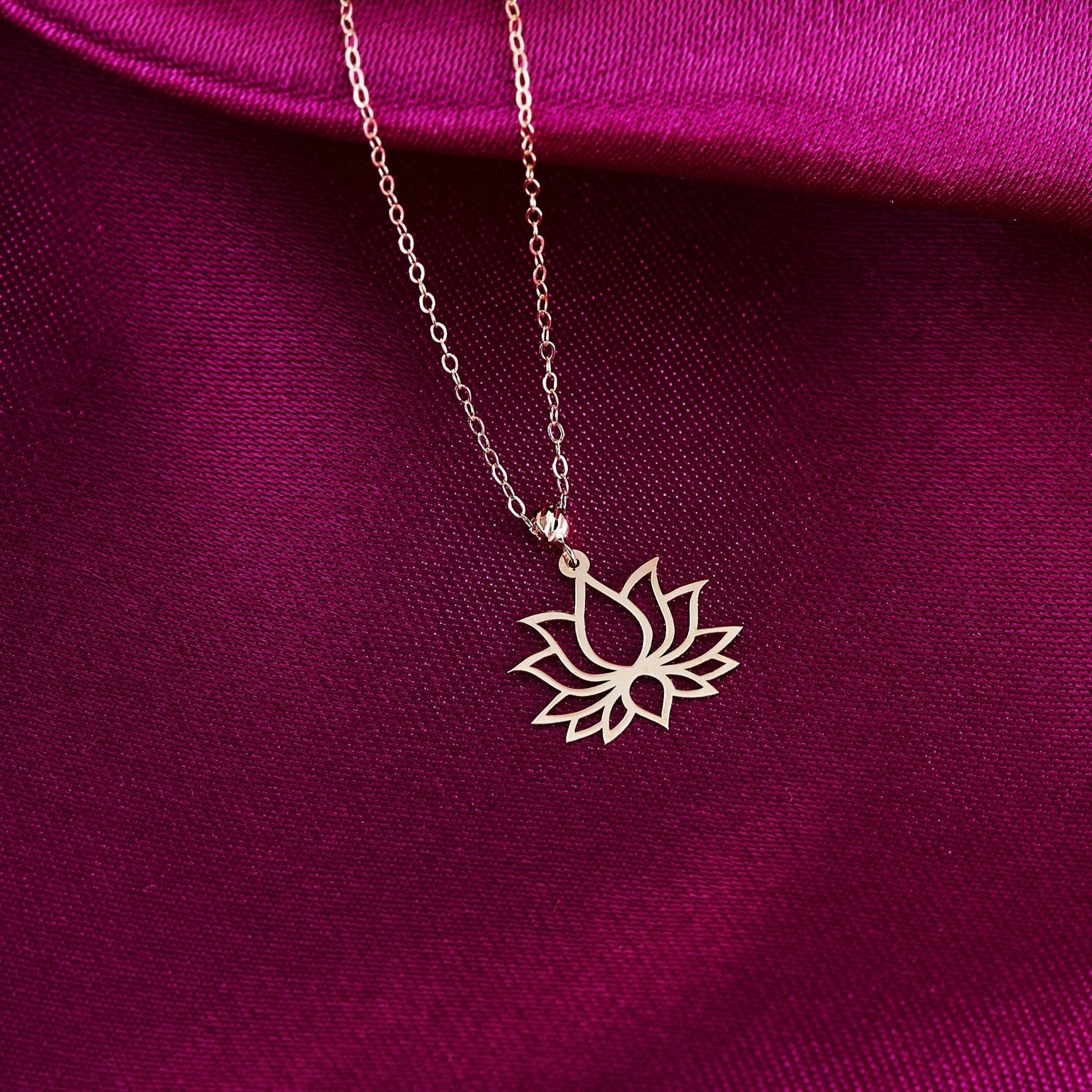 Gold-toned necklace with an openwork lotus flower pendant on a fine oval-link chain, resting on magenta fabric.
