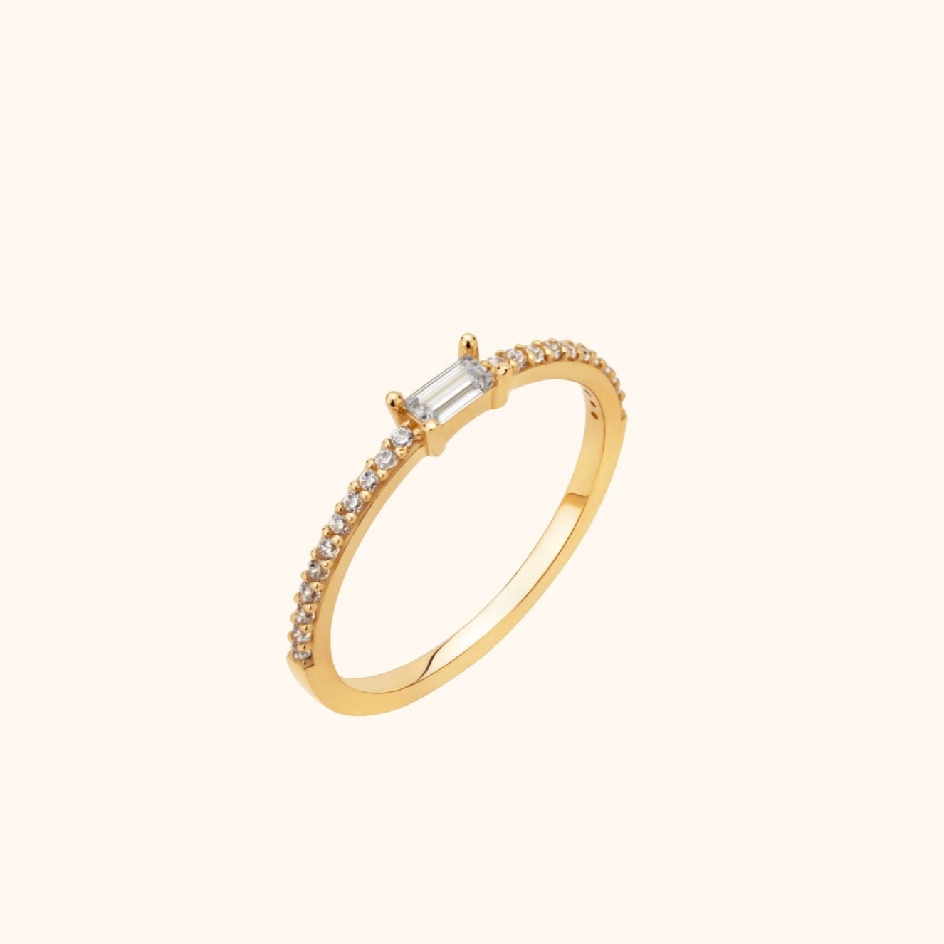Slim gold-toned ring with a rectangular clear center stone and small round clear stones along the band, shown at an angle.