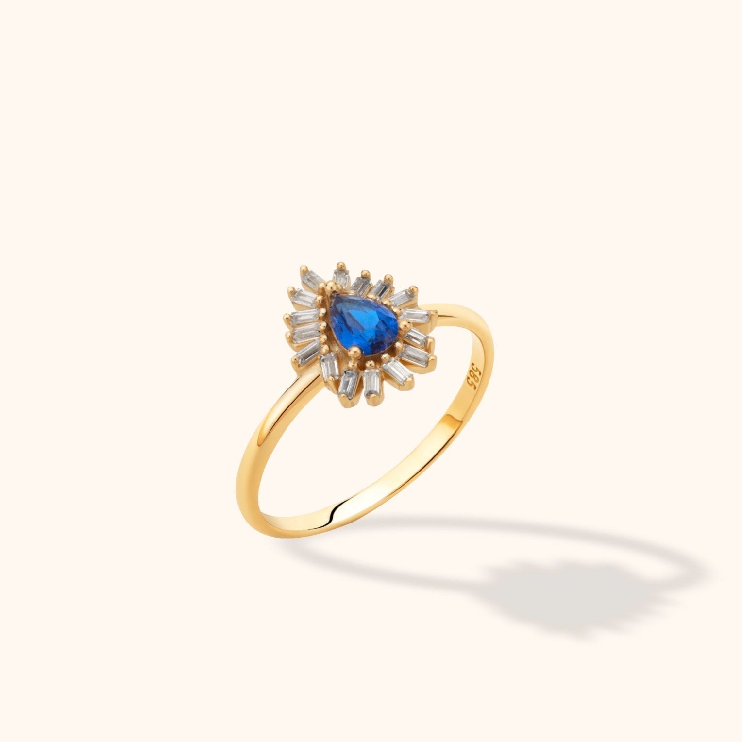 Gold-toned ring with a pear-shaped blue center stone surrounded by clear rectangular stones in a sunburst arrangement.