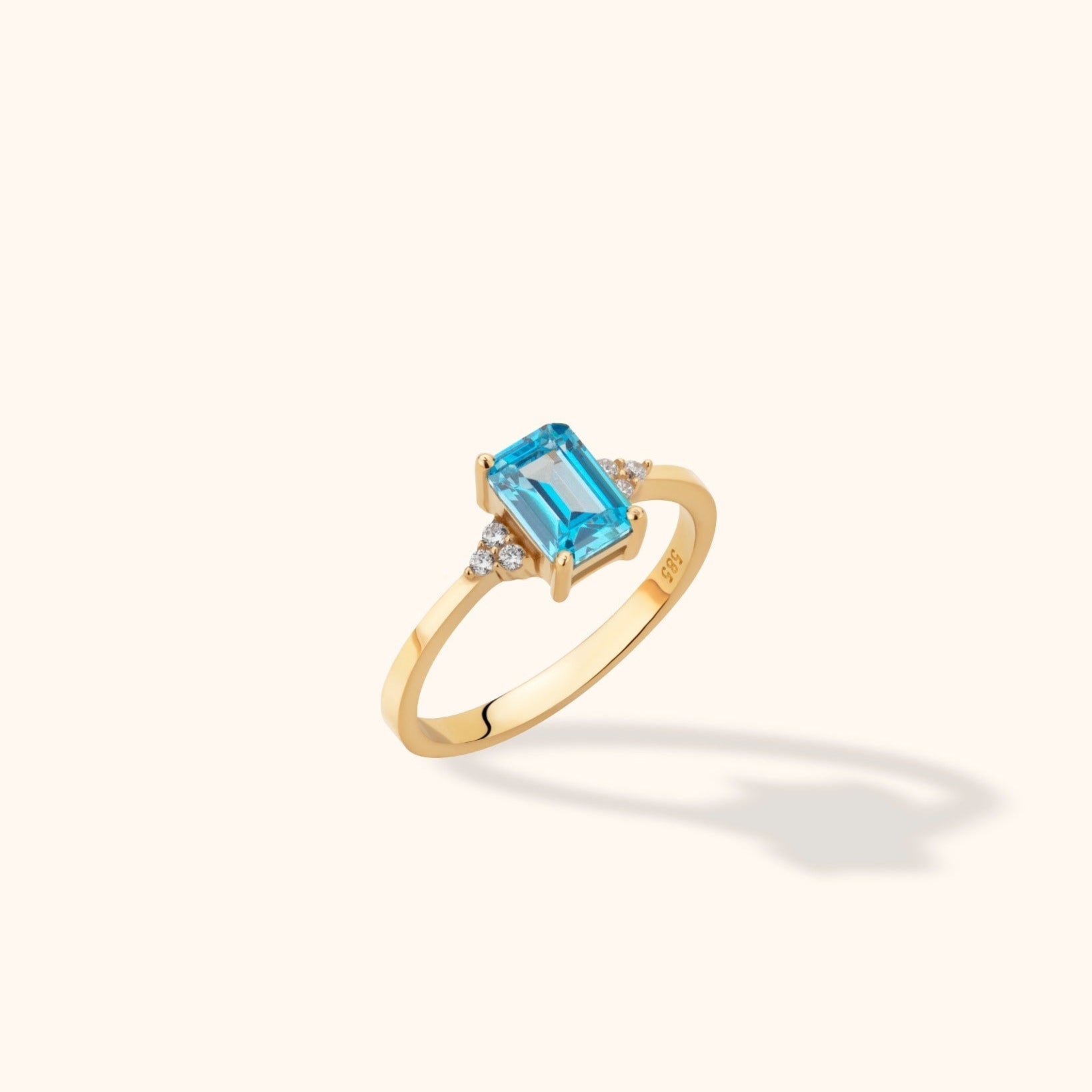 Gold-toned ring with a rectangular faceted blue center stone and clusters of small clear stones on either side.