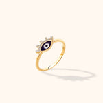 Gold-colored slim ring with a dark blue, white and black eye motif and clear round accents along its upper edge.