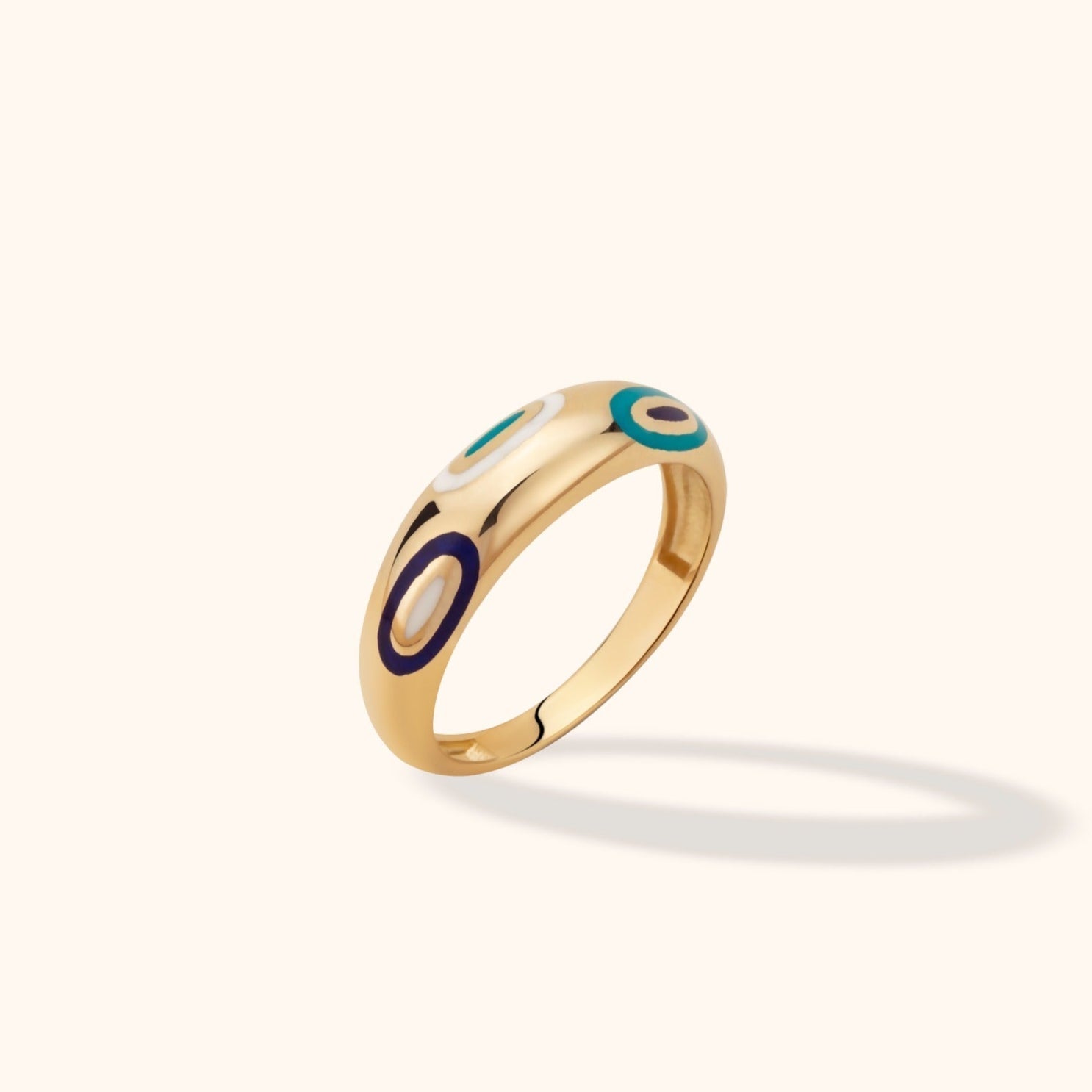 Polished gold-colored ring with turquoise, dark blue and white eye motifs, shown tilted on a pale background.
