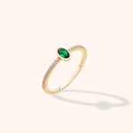 Gold-toned ring with an oval green stone in a smooth bezel and small round clear stones lining the slender band.