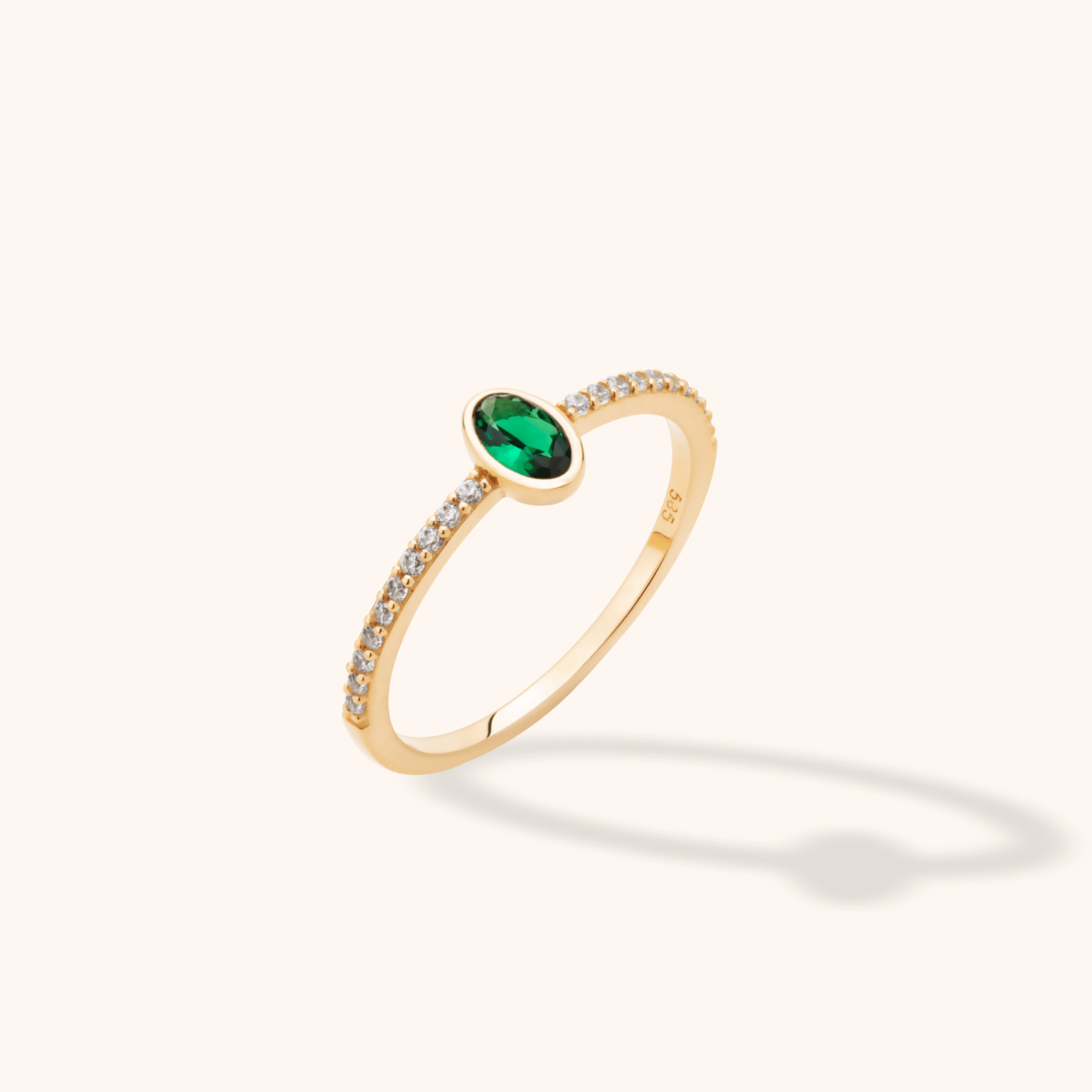 Gold-toned ring with an oval green stone in a smooth bezel and small round clear stones lining the slender band.