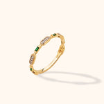 Gold-colored ring with alternating rectangular green stones and elongated settings of small clear round stones on a cream background.
