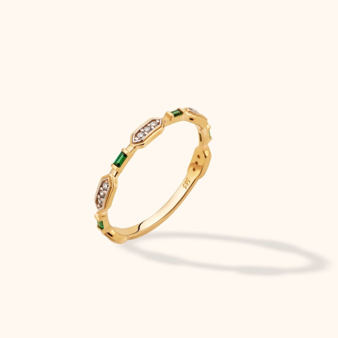 Gold-colored ring with alternating rectangular green stones and elongated settings of small clear round stones on a cream background.