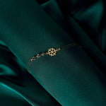 Gold-tone bracelet with a cutout snowflake charm, fine double chains and three clear faceted accents on dark green fabric.