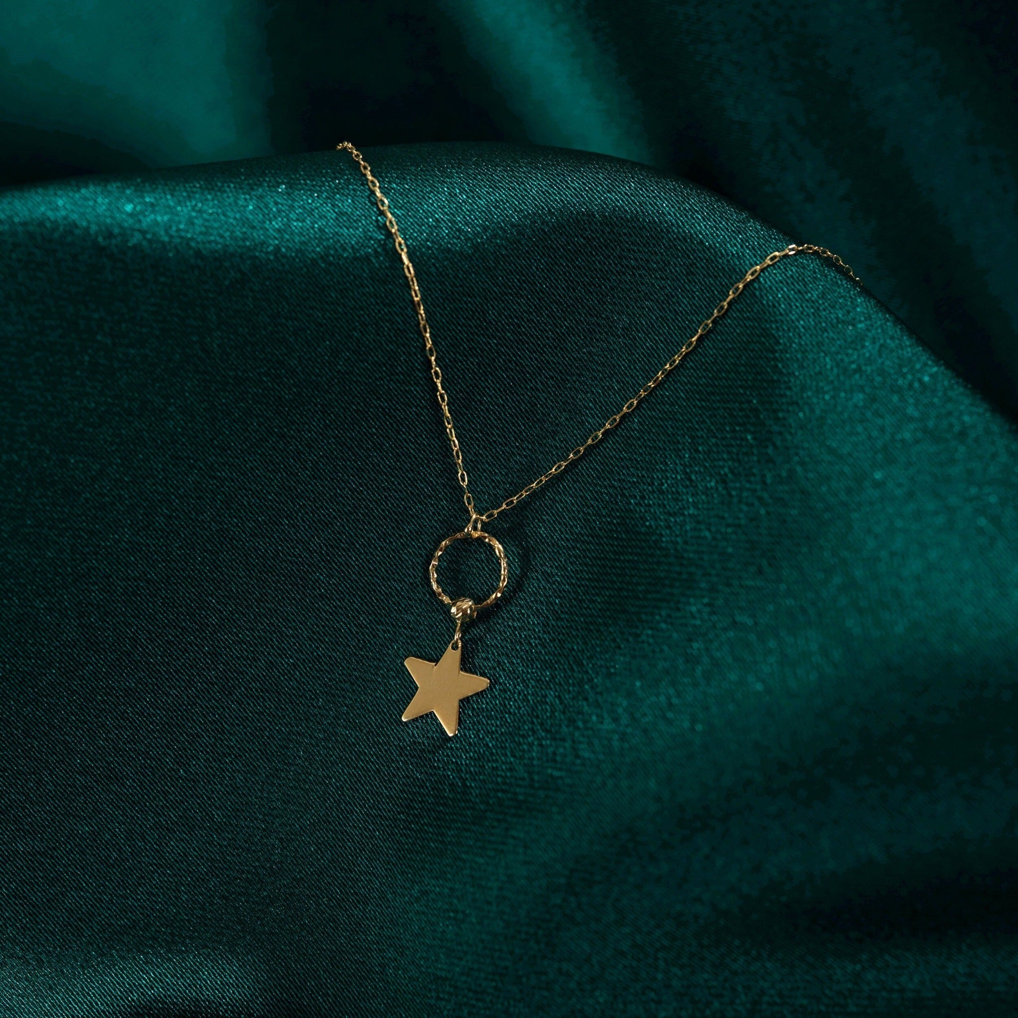 Gold-toned chain necklace with a textured open circle and dangling five-point star on dark teal fabric.