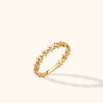 Gold-colored ring with a row of five-pointed stars and small clear round accents, tilted against a cream background.
