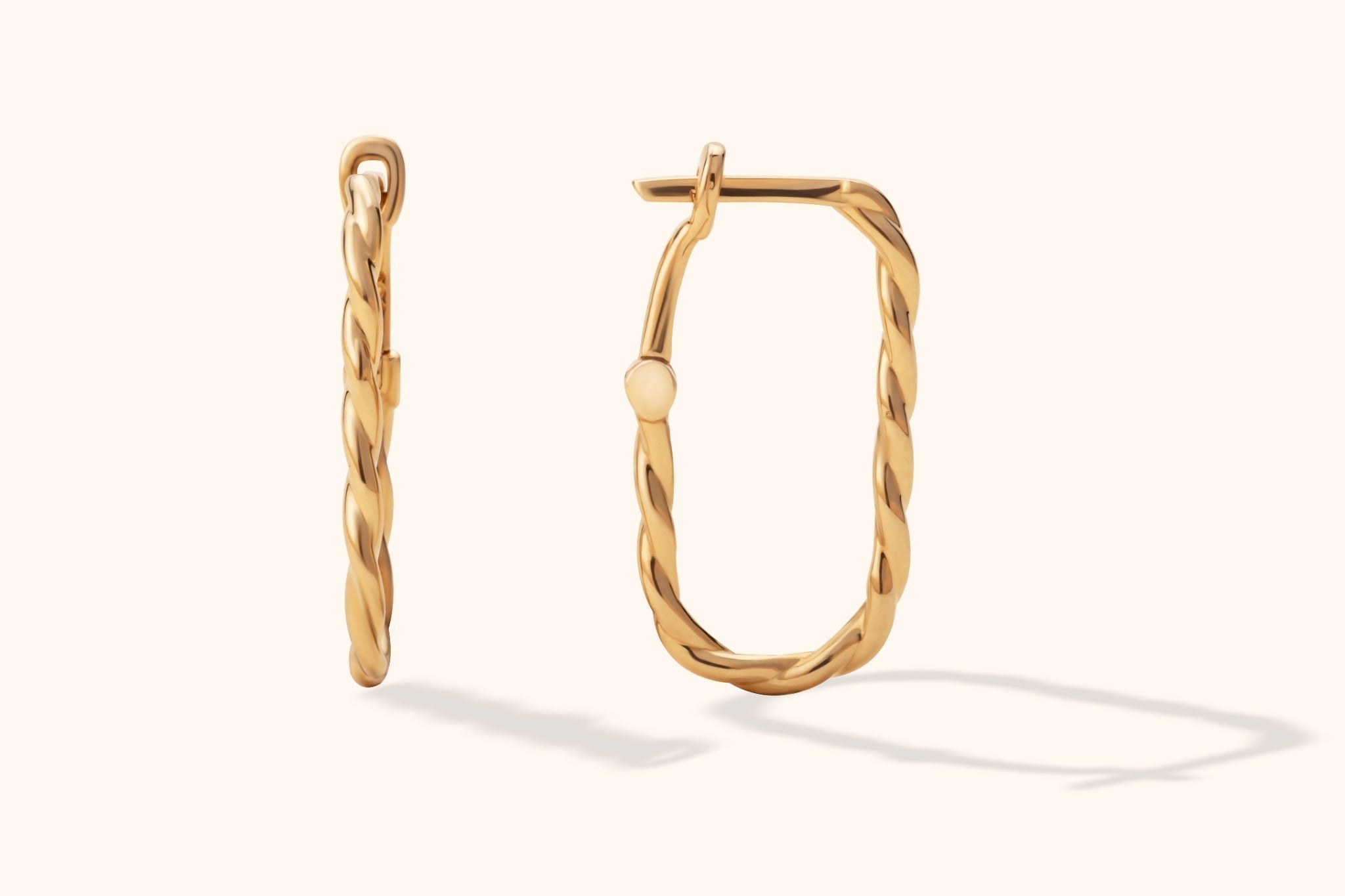 Pair of gold-colored twisted hoop earrings with elongated, rounded rectangular outlines, shown from two angles on a cream background.