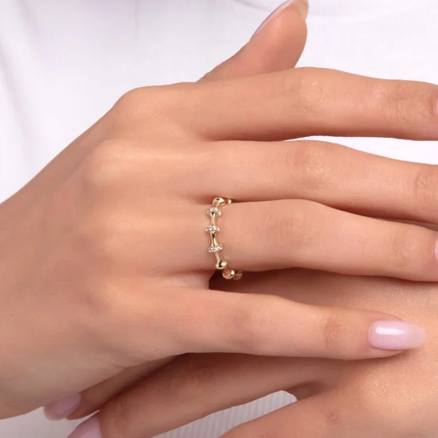 Close-up of a woman's hand wearing a 14K gold ring featuring horizontally set baguette-cut stones linked with gold bead details, complemented by a delicate gemstone bracelet.