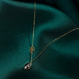 Elegant 14K gold necklace with black onyx teardrop pendant and floral charm on dark green fabric background