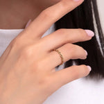 Minimalist gold chain-link ring on a woman's hand with a soft pink manicure, paired with delicate gold bracelets and hoop earrings.

