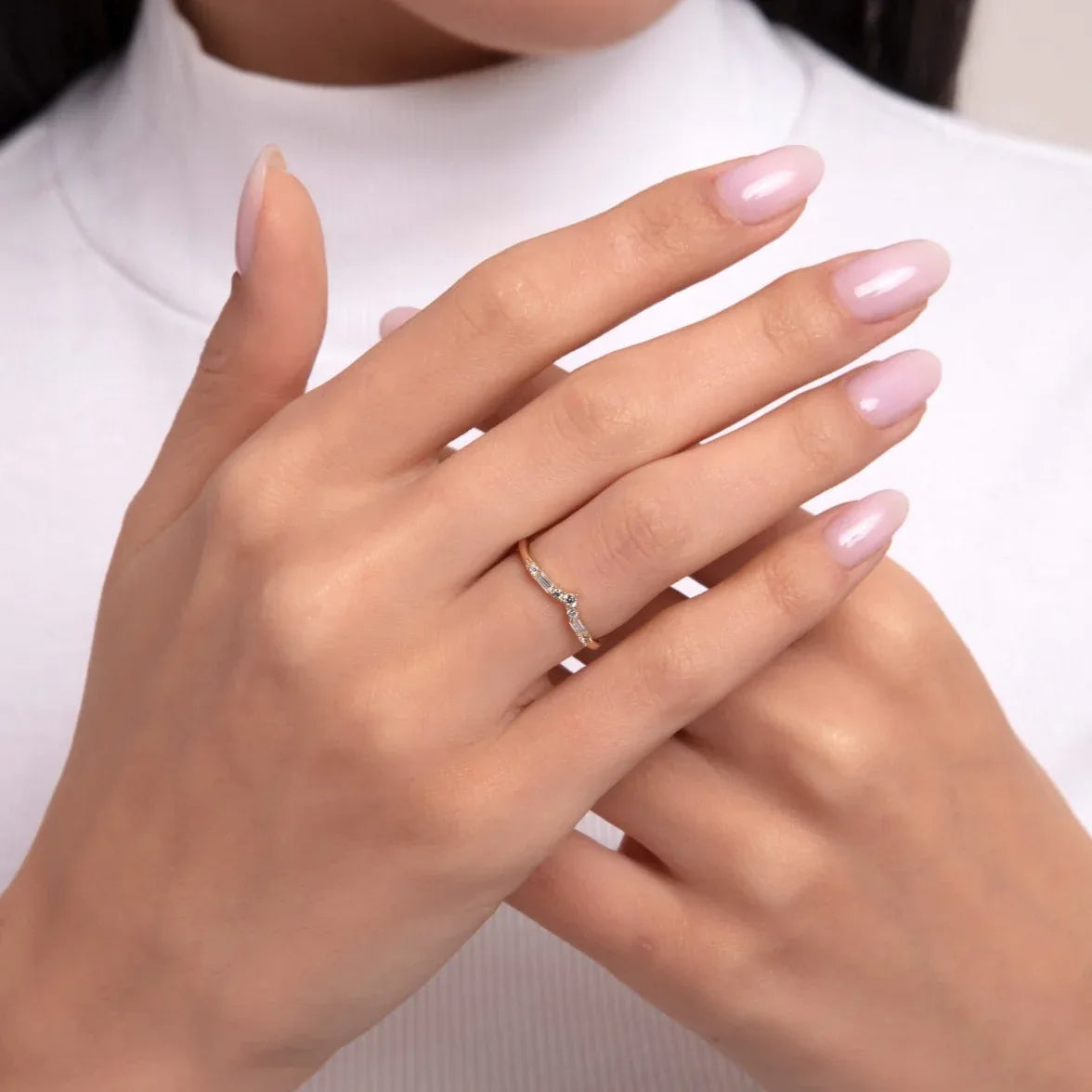 A dainty 14K gold ring with a gentle curve, accented by small diamonds, shown on a hand with soft pink nails in an elegant pose.