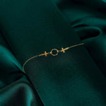 14K gold bracelet with two cross charms and a textured circular centerpiece on deep green fabric.