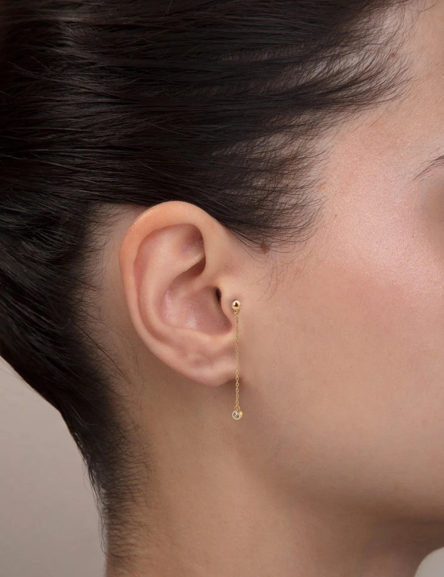 Yakın plan kulak; iç konçta 14 ayar sarı altın zincirli sarkıt piercing, uçta bezel pırlanta.