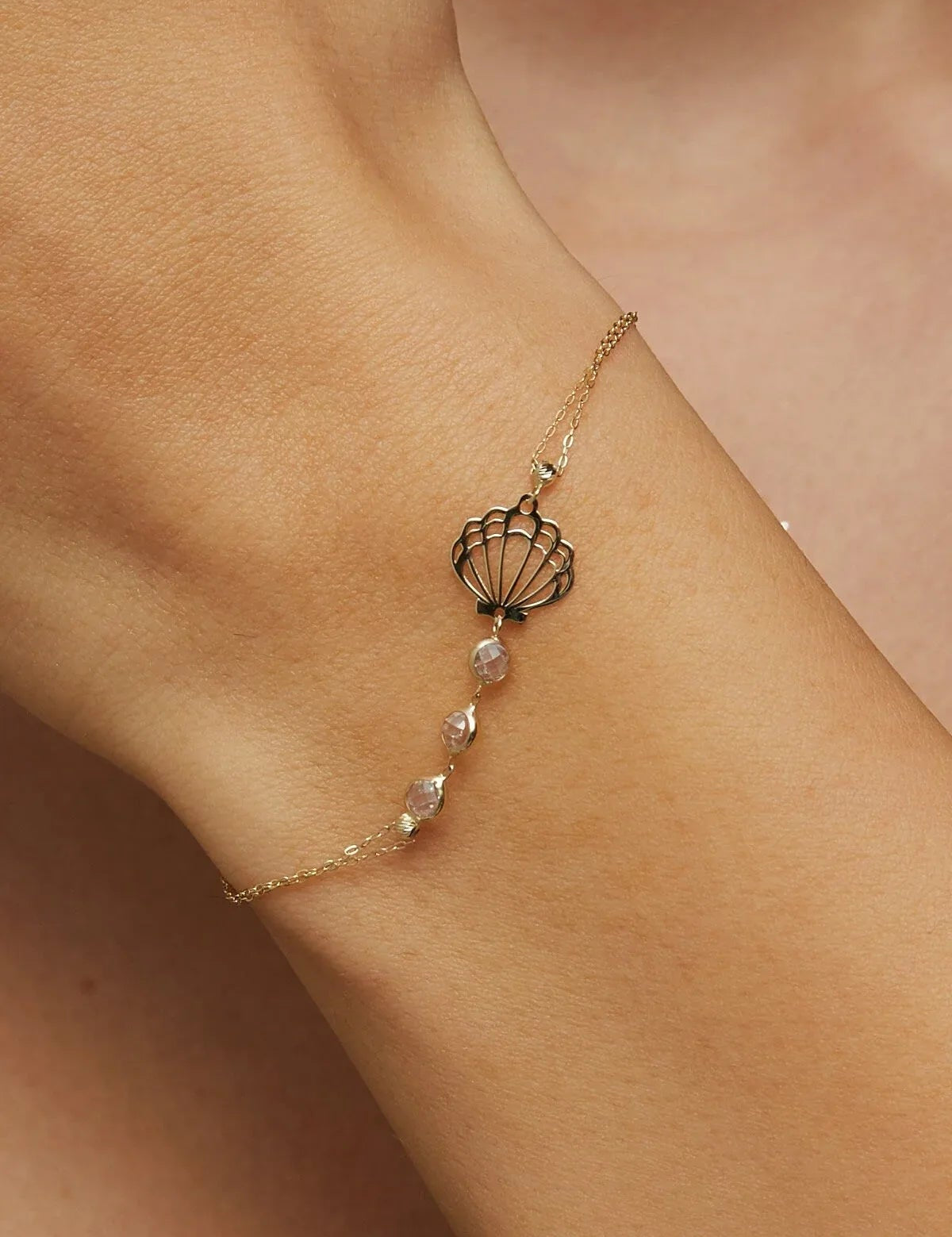 Elegant 14K gold bracelet with a cut-out seashell charm and faceted crystal beads, styled on rich emerald satin