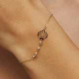 Elegant 14K gold bracelet with a cut-out seashell charm and faceted crystal beads, styled on rich emerald satin