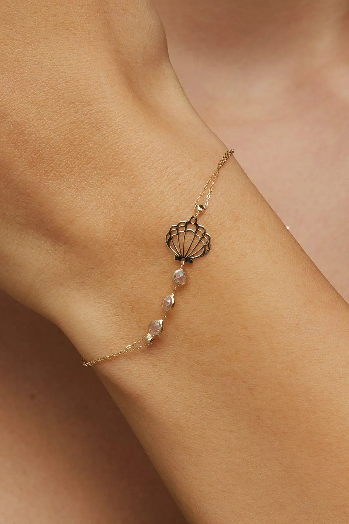 Elegant 14K gold bracelet with a cut-out seashell charm and faceted crystal beads, styled on rich emerald satin