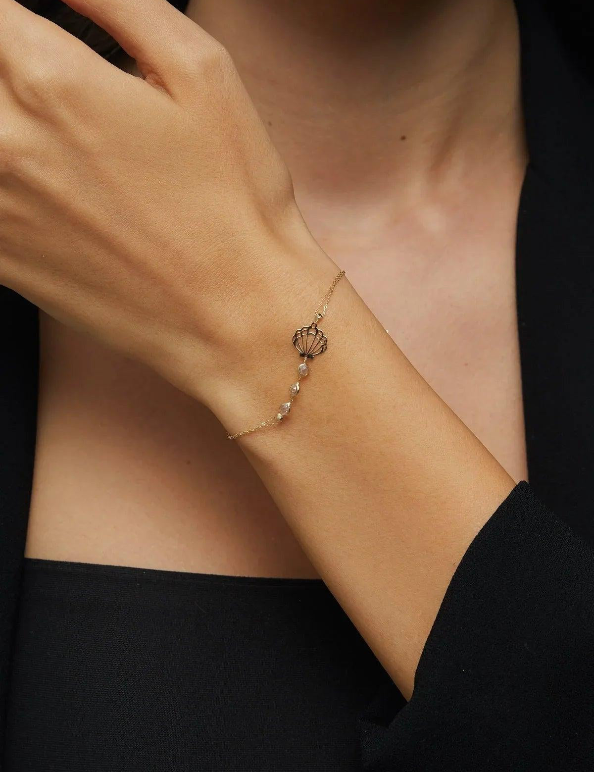 Elegant 14K gold bracelet with a cut-out seashell charm and faceted crystal beads, styled on rich emerald satin