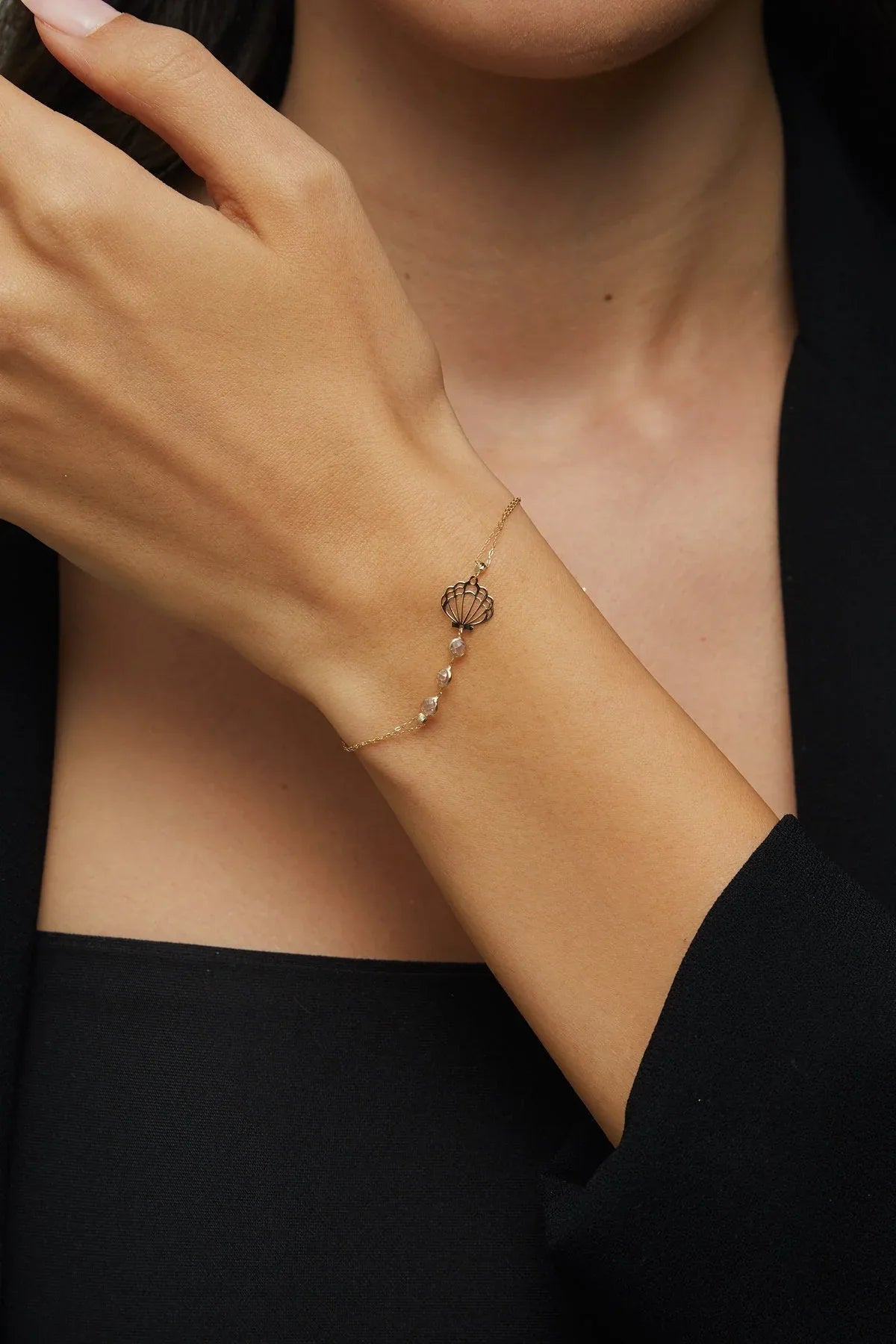 Elegant 14K gold bracelet with a cut-out seashell charm and faceted crystal beads, styled on rich emerald satin