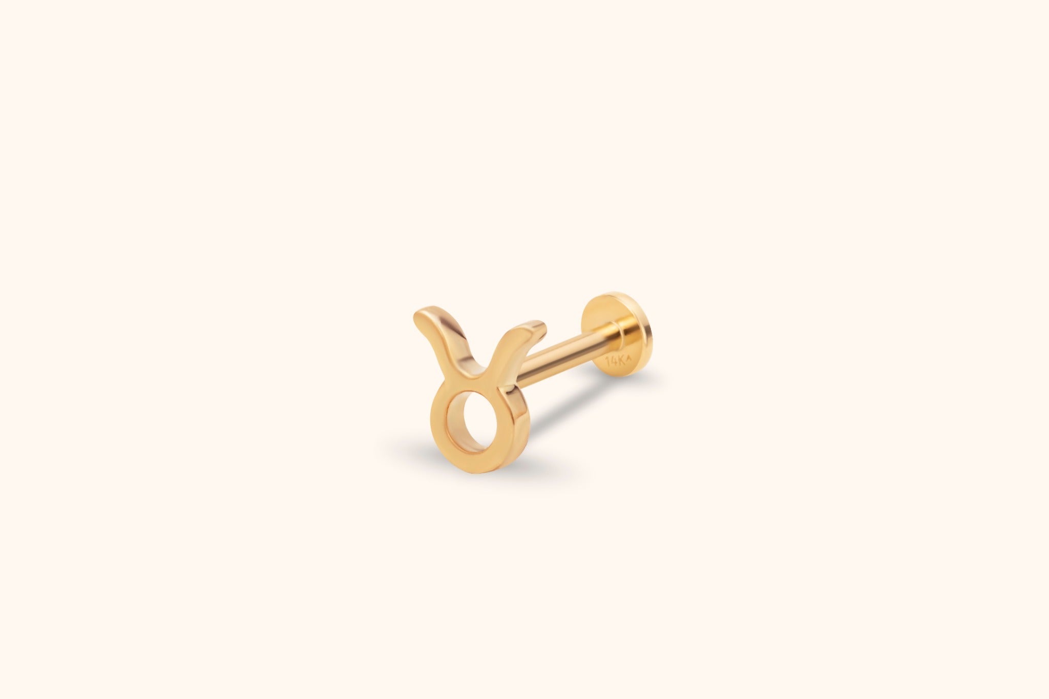 Gold-colored Taurus symbol stud earring with a straight post and round flat back, shown at an angle on a cream background.